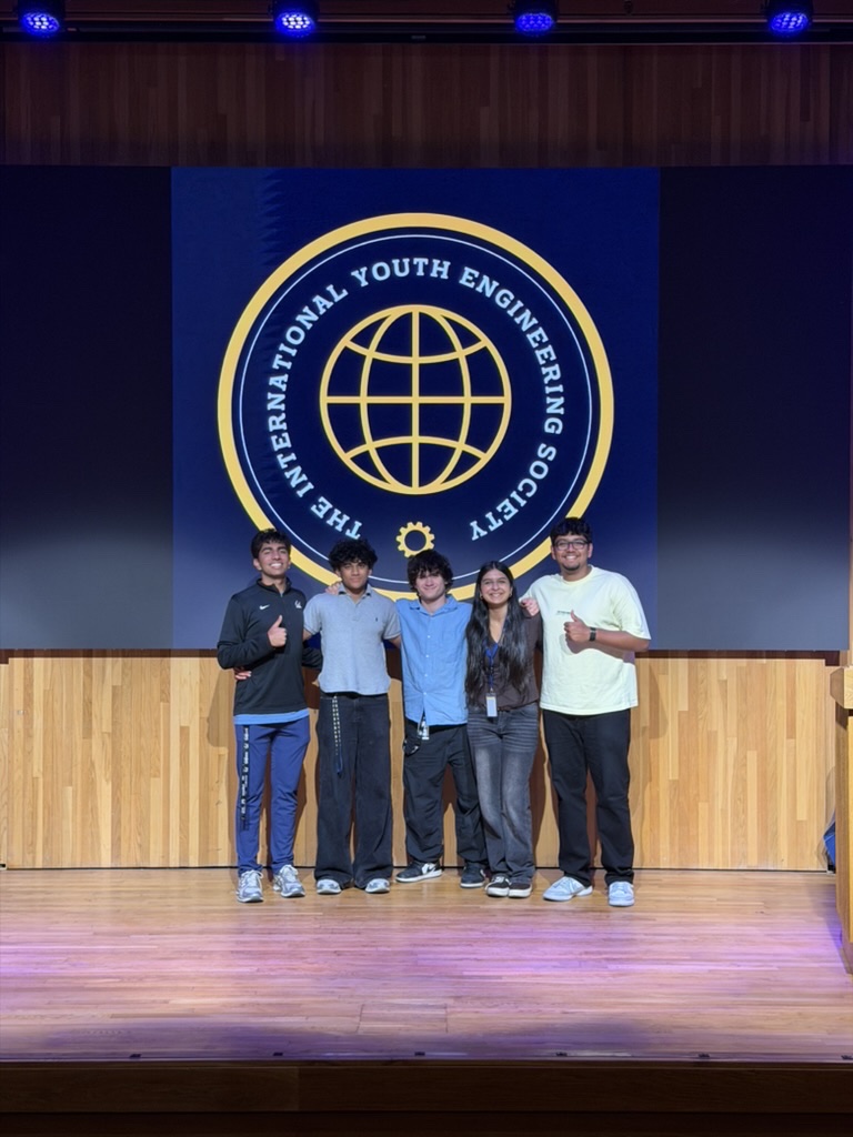 The TIYES founding team on stage in front of the organization emblem: Ahan, Prahalad, Fabian, Aarushi, and Rajdeep
